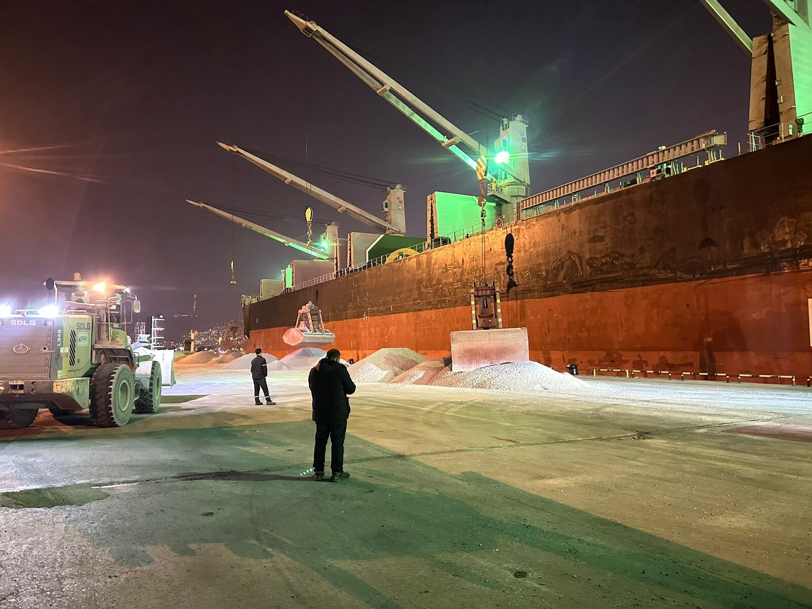 Surveyor observing a night-time cargo discharge operation alongside a bulk carrier